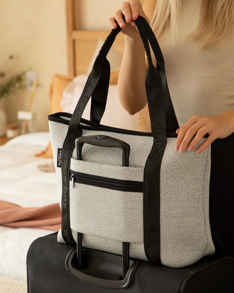 Light marle perforated neoprene travel tote with black handles and luggage sleeve on a suitcase.