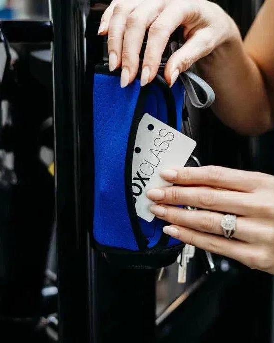 Electric blue magnetic gym caddy holding a phone, keys, and a white "BOXCLASS" card, attached to gym equipment.