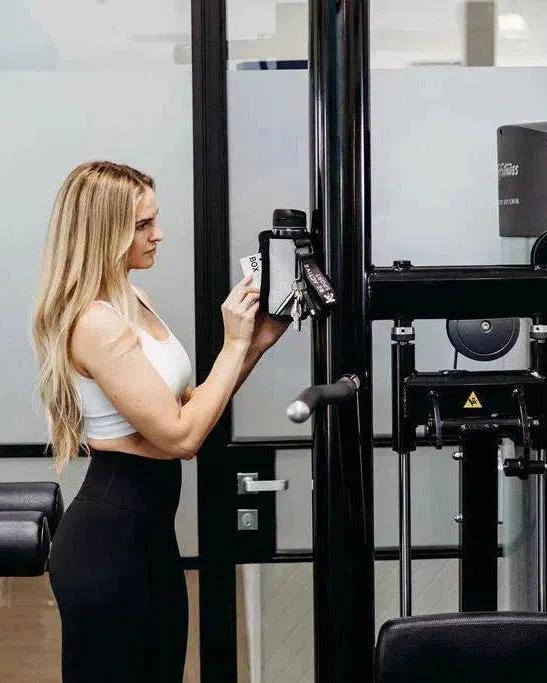 Woman placing phone, keys, and cards into a light marle magnetic gym caddy attached to black gym equipment.
