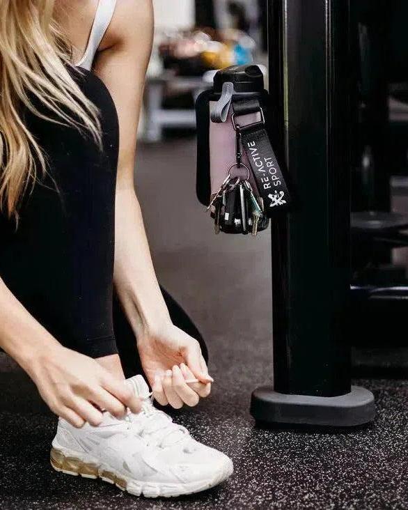 Thistle magnetic gym caddy with keys and phone attached to black gym equipment, next to a person tying white athletic shoes.