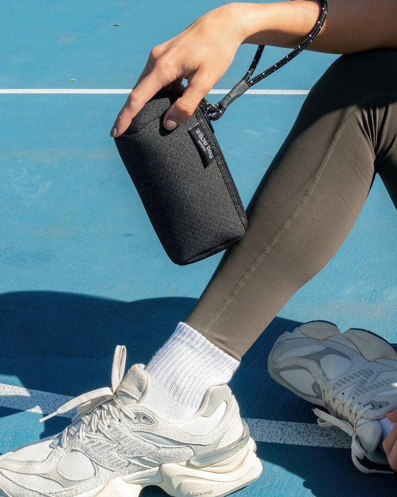 Black denim neoprene wristlet clutch with detachable strap, held by a person in athletic wear.