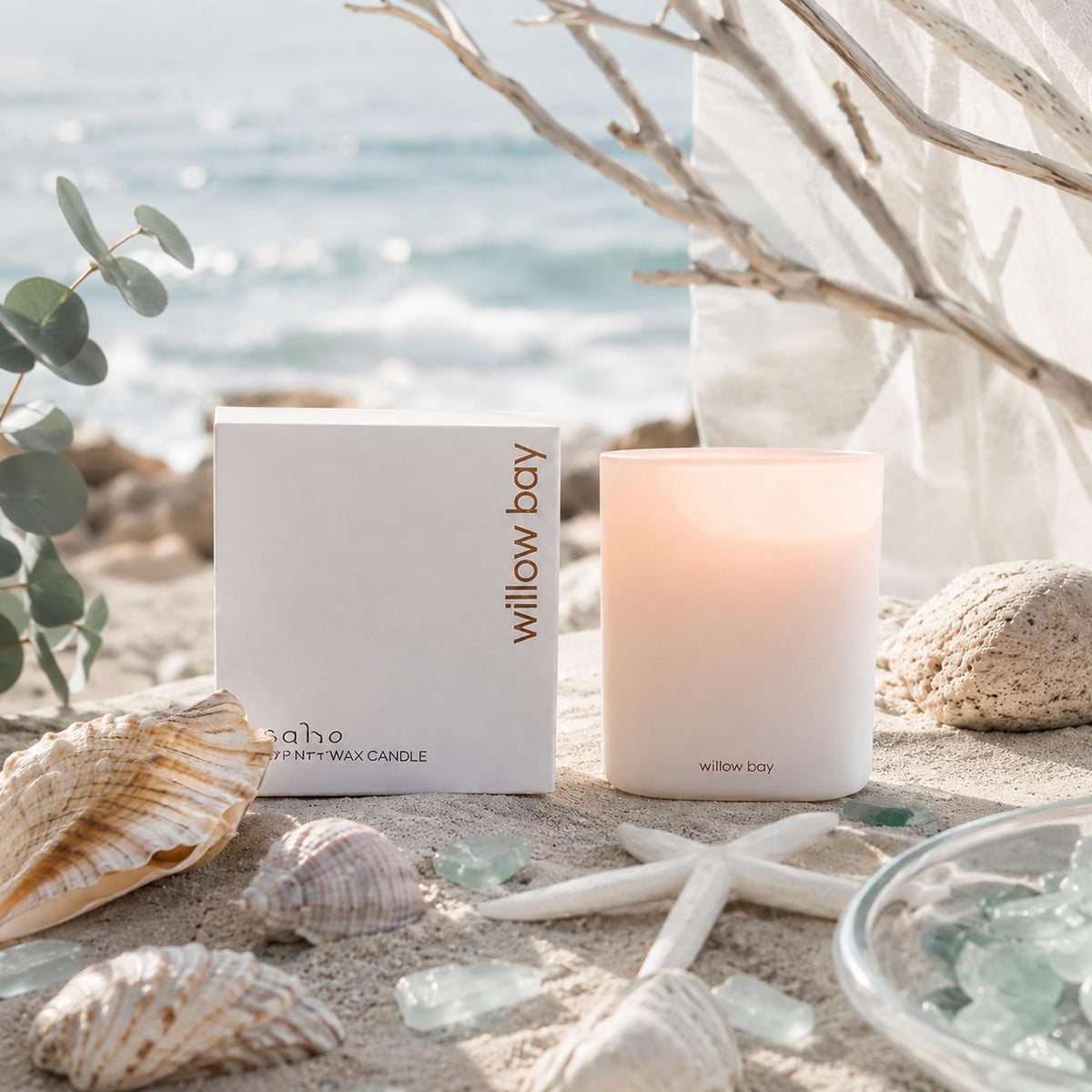 White frosted glass Willow Bay Coastal Drift soy candle with packaging on a sandy beach.
