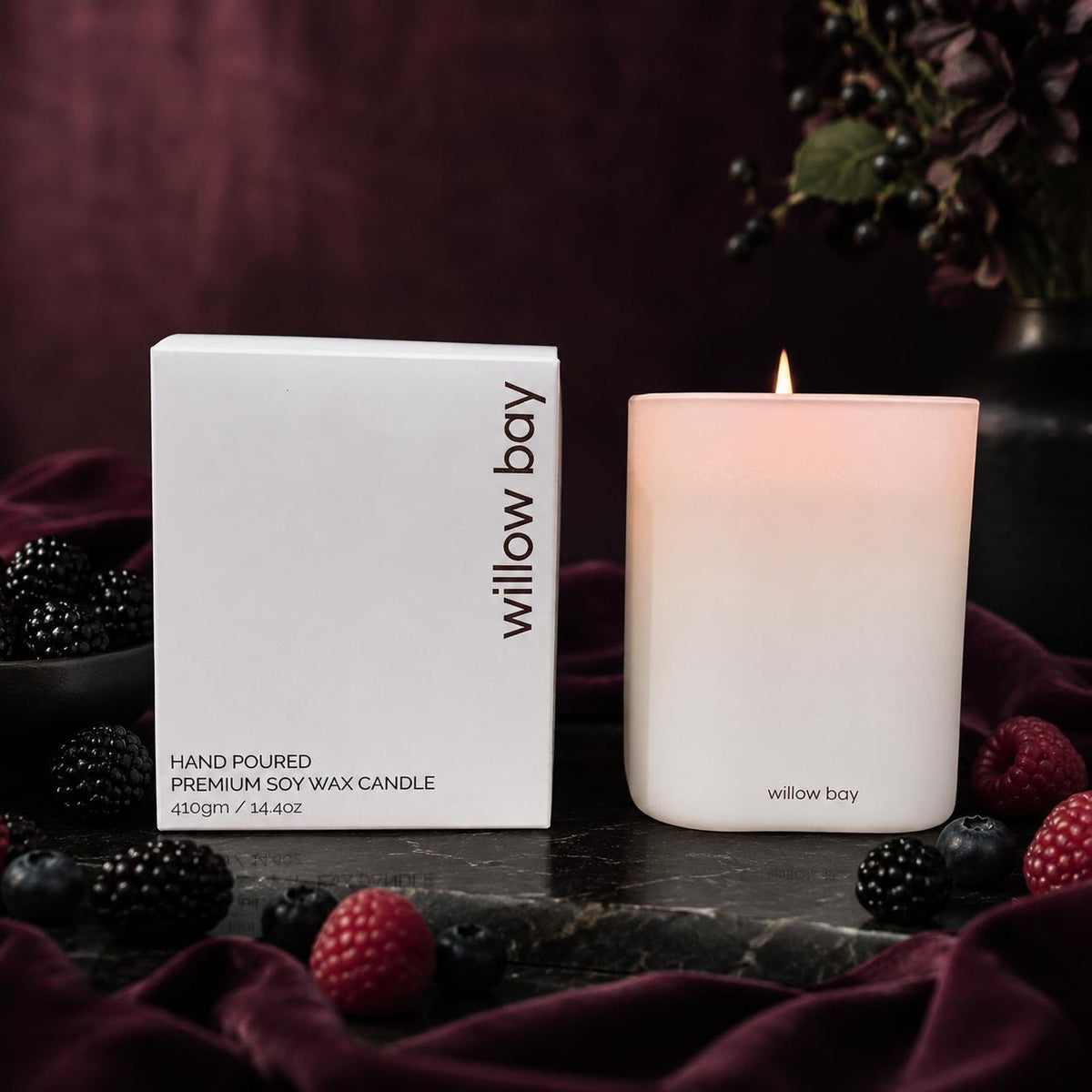 White frosted glass Willow Bay soy candle, 410g, burning next to its box, surrounded by berries.